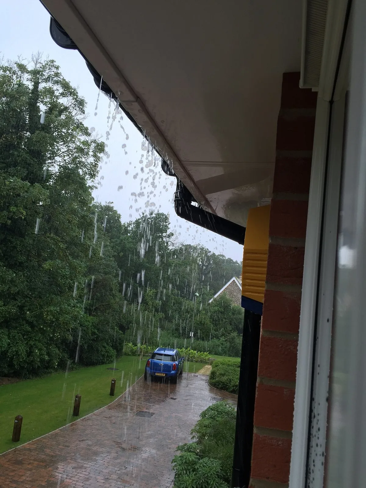 Água de chuva transbordando pela borda de uma calha no beiral de uma casa durante chuva forte