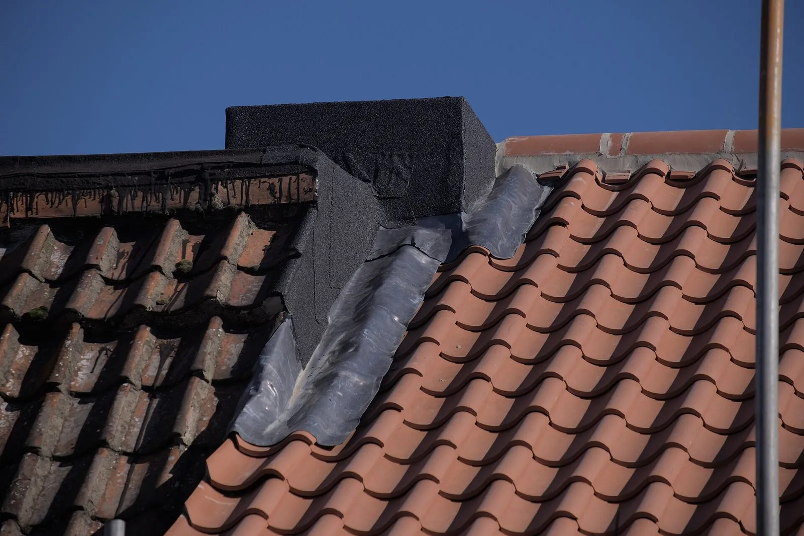 Encontro de telhado de telhas cerâmicas com uma parede de alvenaria escura, vedado por rufo metálico cinza